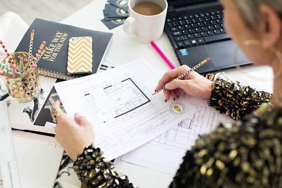 Persona revisando planos arquitectónicos en escritorio con laptop, café y materiales de oficina