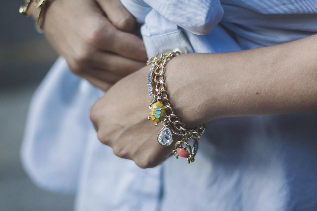Pulsera dorada con dijes coloridos en muñeca de mujer con camisa azul claro