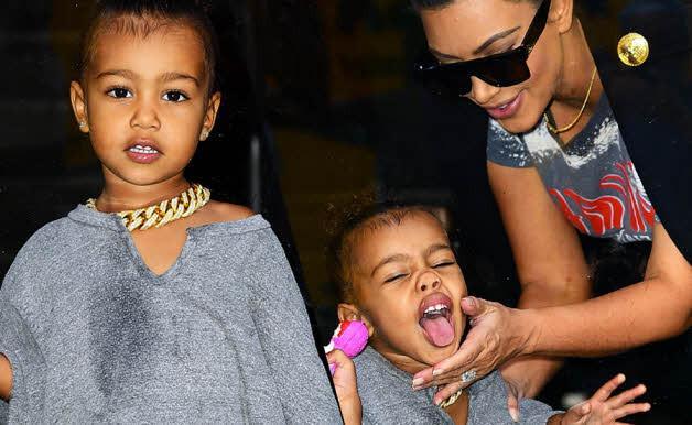 Niña con suéter gris y collar dorado, y mujer con gafas oscuras y camiseta mientras cuida a la niña