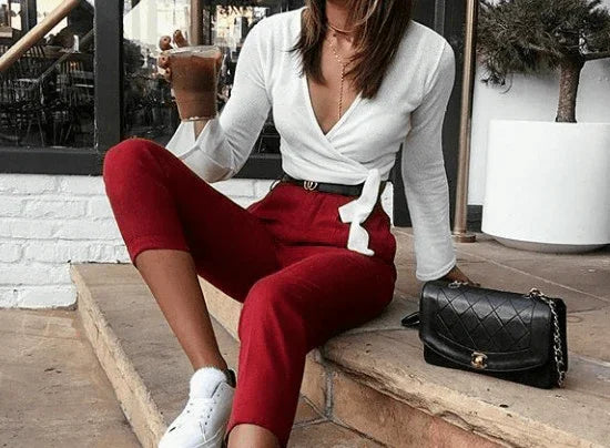 Mujer sentada en escalón con pantalones rojos, blusa blanca, sneakers blancas y bolso negro junto a ella