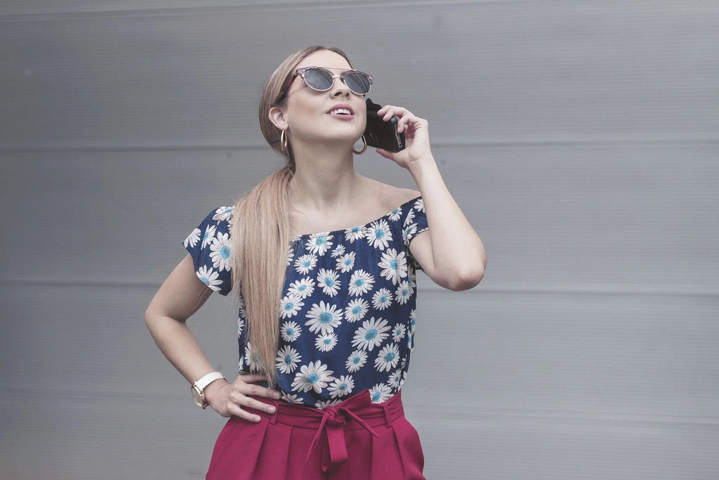 Mujer joven con blusa floral y pantalones rojos hablando por teléfono con gafas de sol