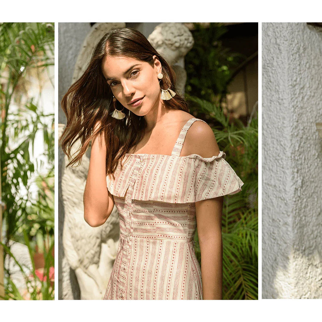 Mujer con vestido beige de rayas y volantes, pendientes grandes, con fondo de plantas y estatua blanca