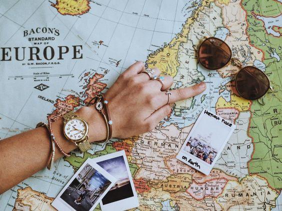 Mano con reloj dorado y pulseras sobre mapa antiguo de Europa, fotos instantáneas y gafas de sol