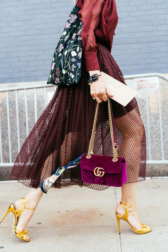 Mujer con falda midi de malla bordó, sandalias doradas, bolso Gucci morado y bolsa de flores calle urbana