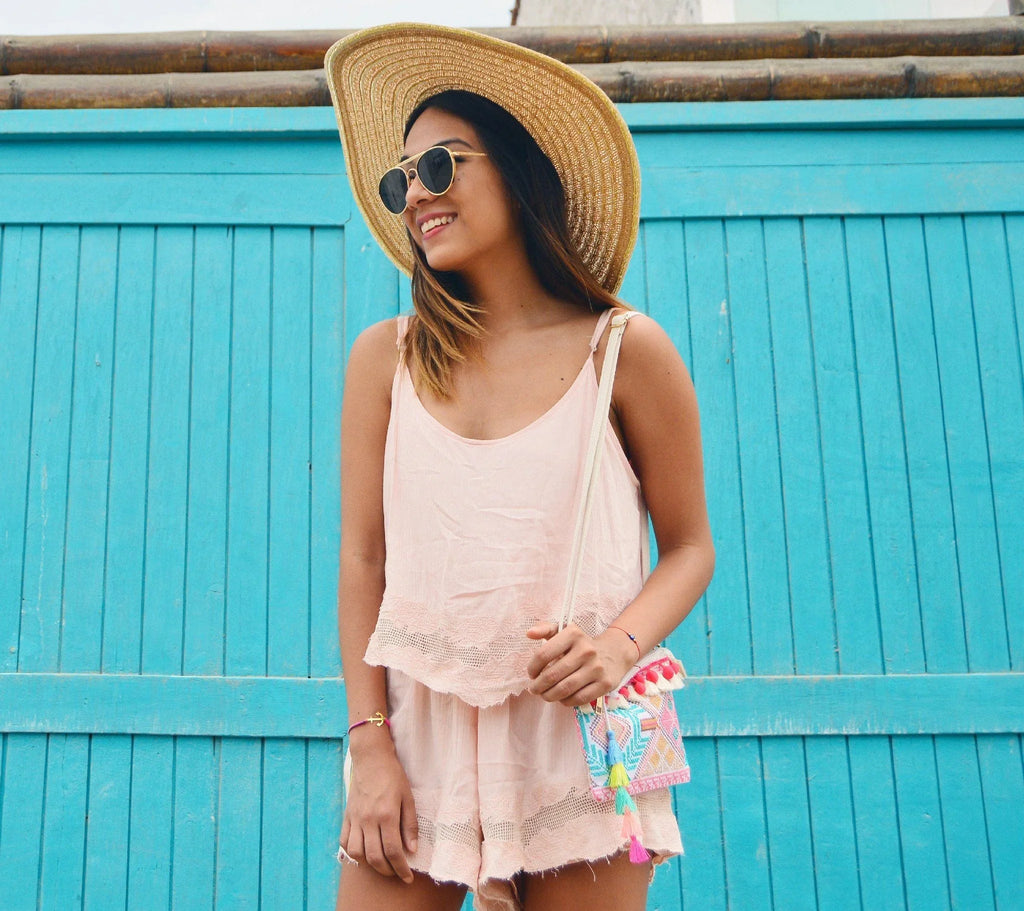 Mujer con sombrero, gafas de sol y vestido rosa frente a puerta azul en ambiente soleado
