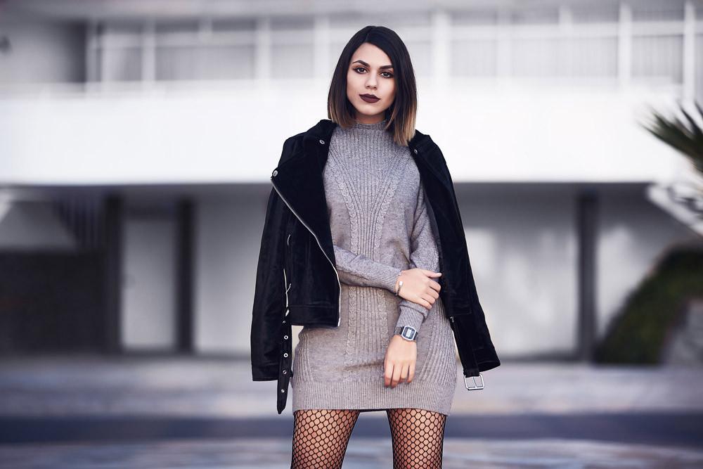 Mujer joven con vestido gris de punto, chaqueta negra y medias de red en entorno urbano moderno