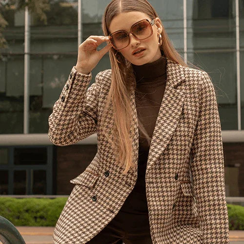 Mujer con gafas de sol y blazer de pata de gallo marrón en entorno urbano moderno