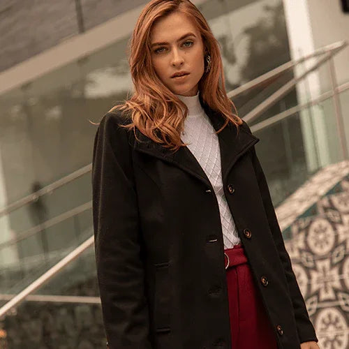 Mujer con abrigo negro y pantalón rojo posando en escaleras modernas de edificio con diseño minimalista