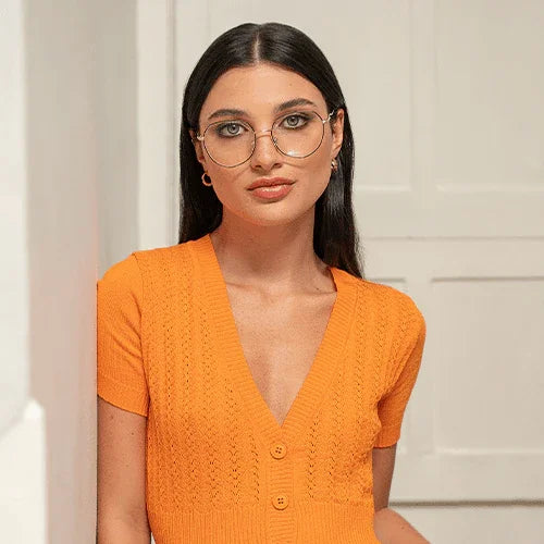 Mujer con gafas grandes y cabello lacio vestido con suéter naranja de botones en fondo blanco