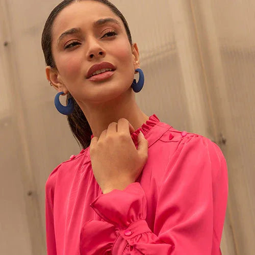 Retrato de mujer con blusa rosa y aretes azules, fondo neutro, estilo moderno y elegante