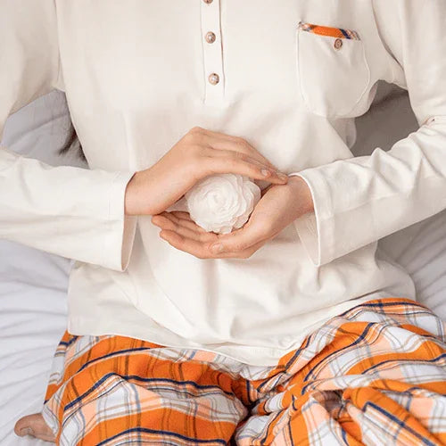 Persona en pijama blanco y pantalones a cuadros naranja sosteniendo una flor blanca en las manos