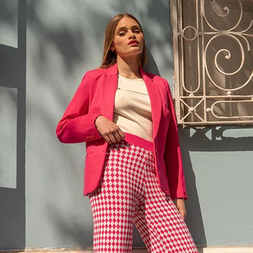 Mujer con blazer rosa y pantalones estampados de cuadros rojos y blancos contra pared azul