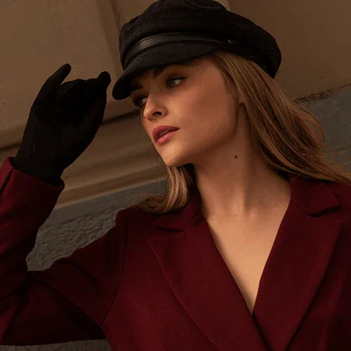 Mujer con boina negra y guantes negros vistiendo un abrigo burdeos elegante, fondo neutro