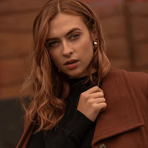 Mujer joven con cabello castaño, abrigo marrón y suéter negro en fondo de madera, moda otoño