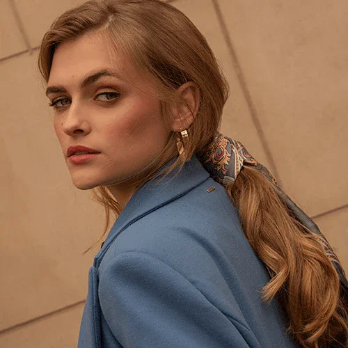 Mujer con maquillaje natural, blazer azul y pañuelo estampado en el cabello, fondo neutro beige