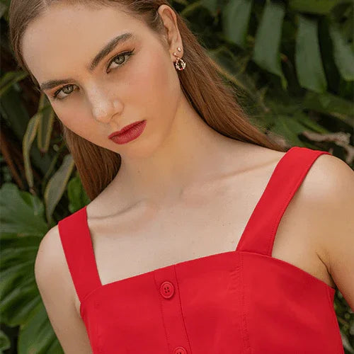 Mujer joven con vestido rojo de tirantes y labios rojos, fondo de hojas verdes