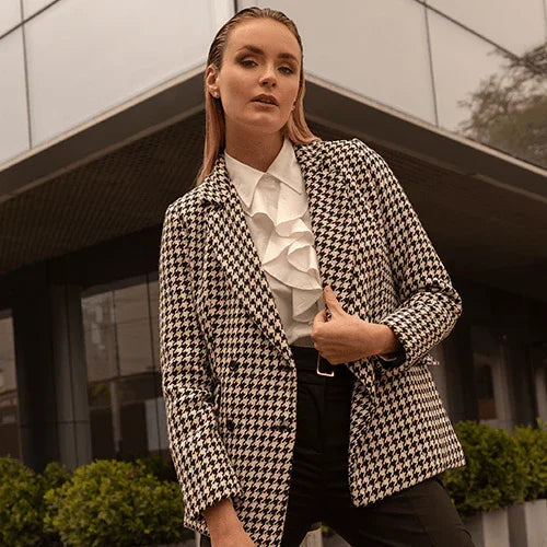 Mujer con blazer de pata de gallo y blusa blanca con volantes en entorno urbano moderno