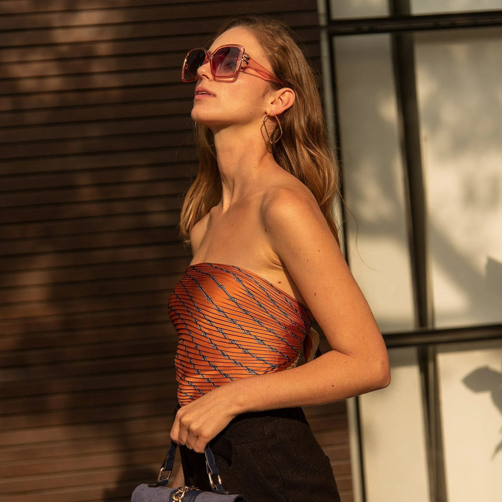 Mujer con gafas de sol grandes y top naranja sin tirantes posando con bolso azul al aire libre