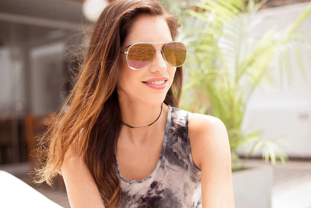 Mujer sonriente con gafas de sol aviador y blusa sin mangas en ambiente exterior con plantas