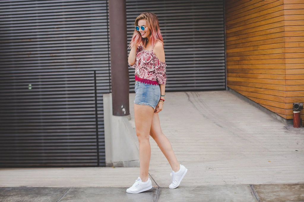 Mujer con cabello rosa y gafas de sol azules caminando en ropa casual urbana con camiseta y shorts