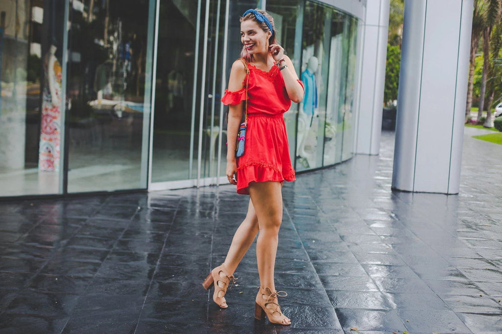 Mujer joven con vestido rojo y sandalias de tacón caminando frente a escaparate moderno en ciudad