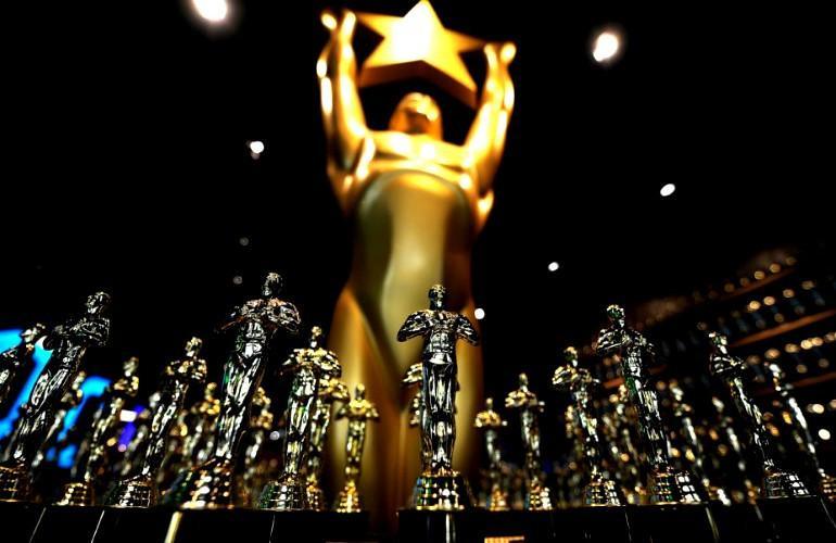 Estatuillas doradas de premios en primer plano con gigante figura dorada sosteniendo una estrella en fondo oscuro