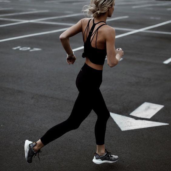 Mujer corriendo en espacio de estacionamiento con ropa deportiva negra y zapatillas grises