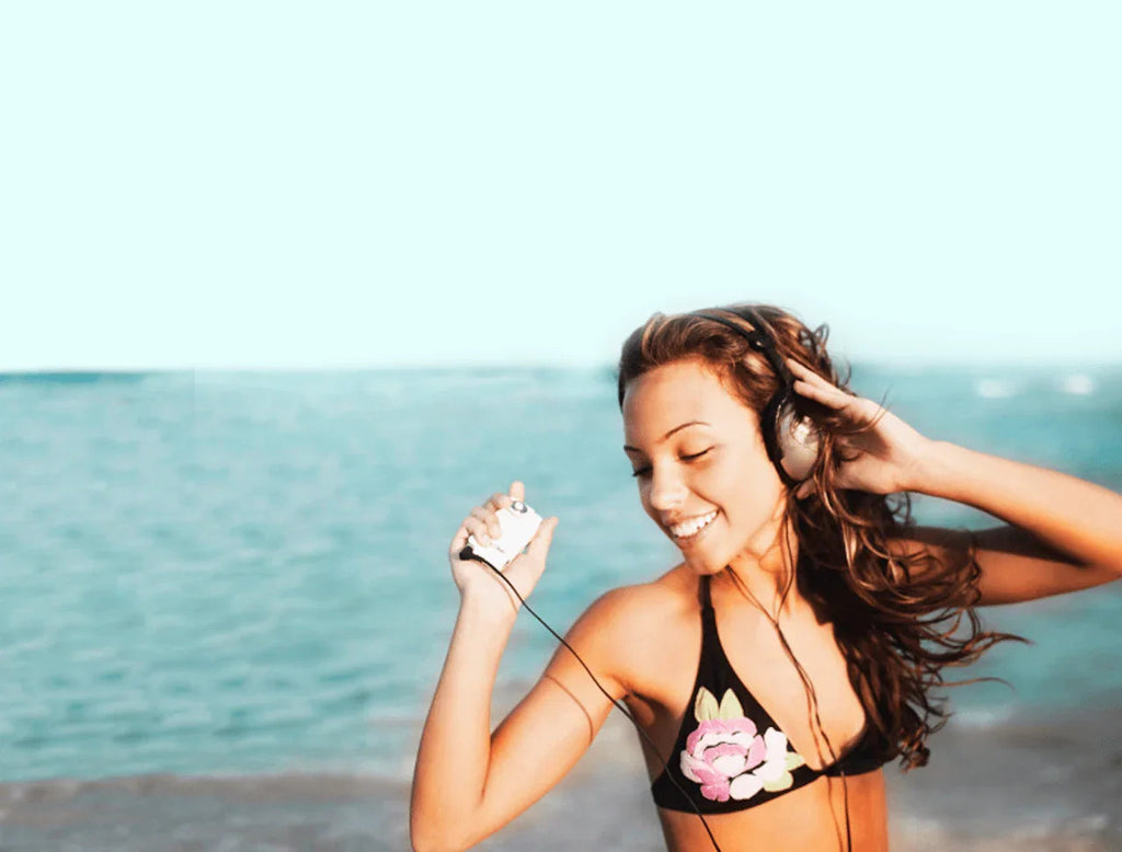 Mujer sonriente con auriculares y reproductor de música en la playa junto al mar
