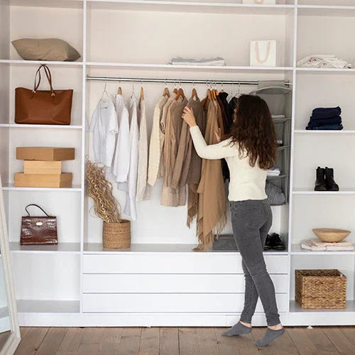 Mujer revisando ropa beige y blanca en armario moderno blanco con accesorios organizados
