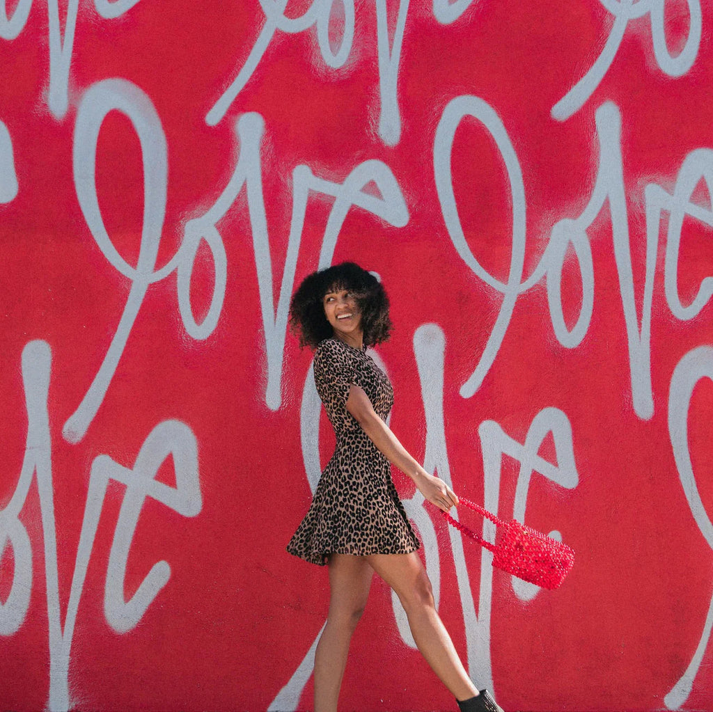 Mujer sonriente con vestido animal print y bolso rojo frente a muro rojo con grafiti "love"