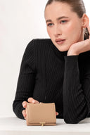 Mujer con suéter negro sostiene cartera beige minimalista, fondo blanco