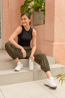 Mujer joven sonriente con ropa deportiva negra y verde sentada en escaleras con botella blanca en mano