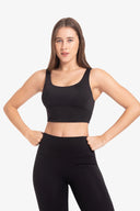 Mujer joven con top deportivo negro y leggings negros en fondo blanco, ropa fitness