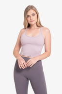 Mujer joven con top deportivo lila y leggings gris en fondo blanco, moda fitness mujer