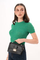 Mujer con blusa verde de punto y jeans oscuros sosteniendo bolso pequeño negro con cierre dorado