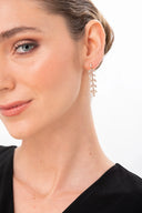 Mujer con pendientes colgantes dorados con diseño de hojas y vestido negro en fondo blanco