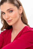 Mujer con maquillaje natural y pendientes dorados de aro, viste blusa roja de manga larga