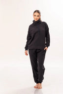 Mujer con ropa casual negra de felpa, suéter cuello alto y pantalones cómodos, fondo blanco