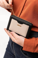 Mano sosteniendo monedero negro y beige con cremallera y cadena dorada sobre camisa naranja y jeans