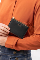 Persona con camisa naranja y jeans sosteniendo cartera negra de mano MOXX