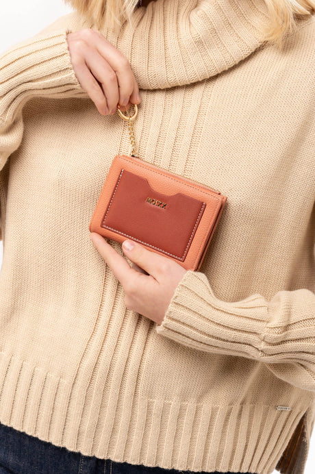 Cartera rosa y marrón con llavero dorado en manos de mujer con suéter beige de punto