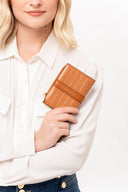 Mujer con camisa blanca sostiene cartera marrón de cuero con textura y cierre dorado